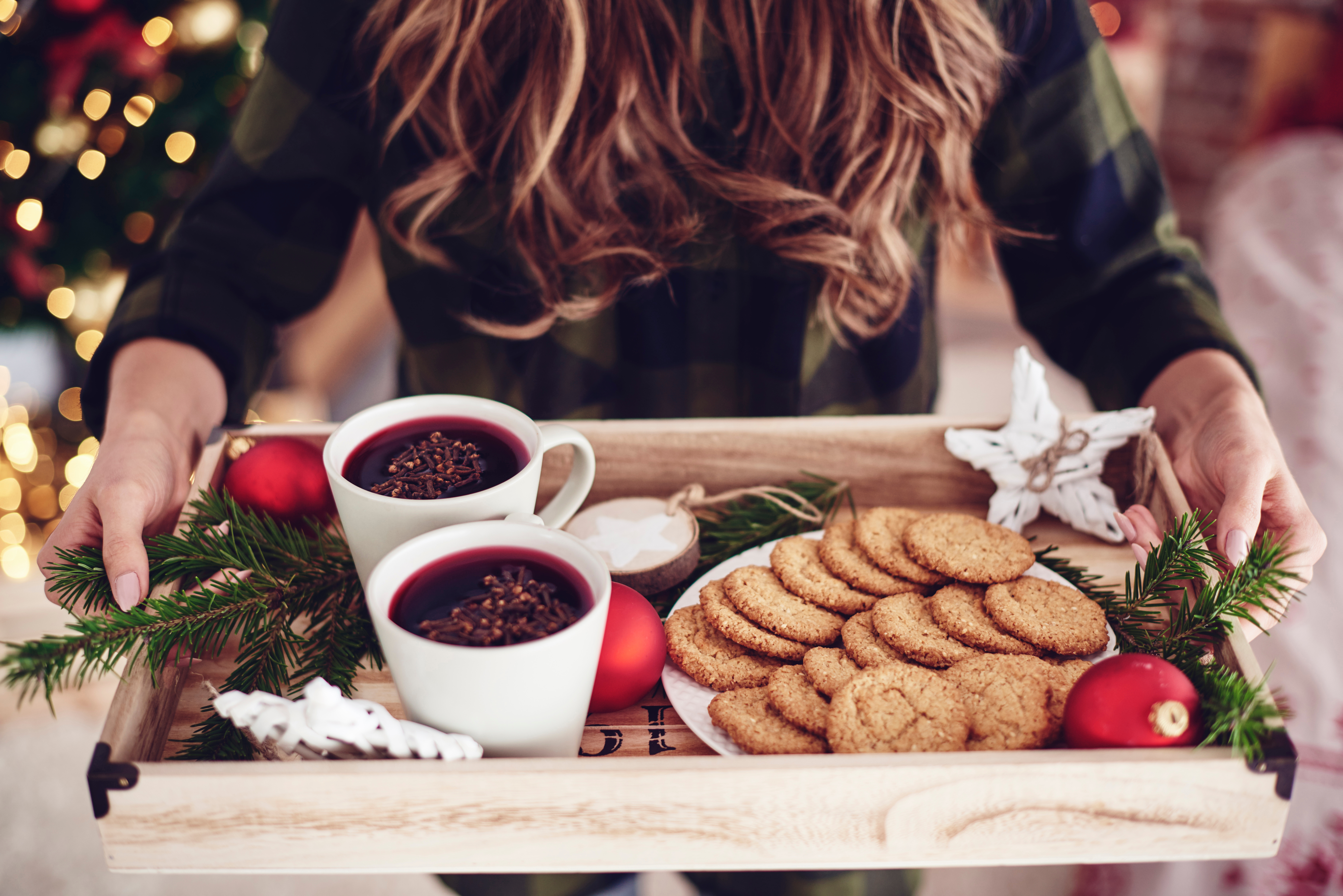 A woman holds a tray with festive cookies and mulled wine